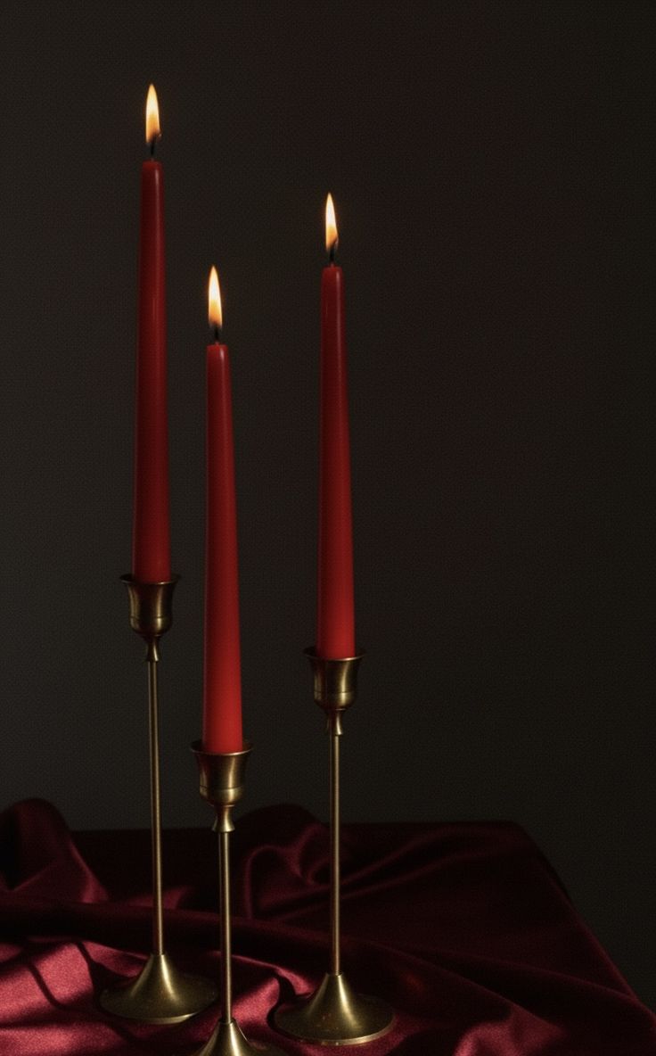 Three lit red taper candles in brass holders on deep crimson silk